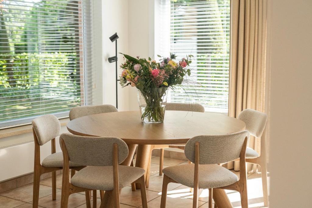 une table à manger avec des chaises et un vase de fleurs dans l'établissement Le petit château by Kasteel Ter Wallen, à Iseghem