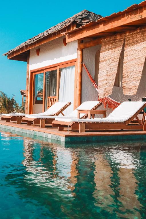 a house with a row of lounge chairs on the water at Villa Caraúbas in Camocim