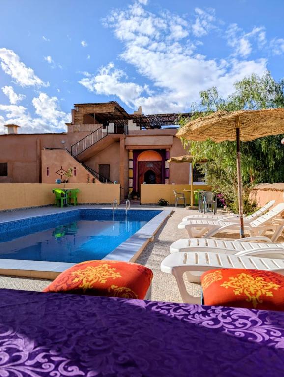 a villa with a swimming pool with chairs and an umbrella at Auberge Restaurant TISSILI " Oasis de Fint" in Fint