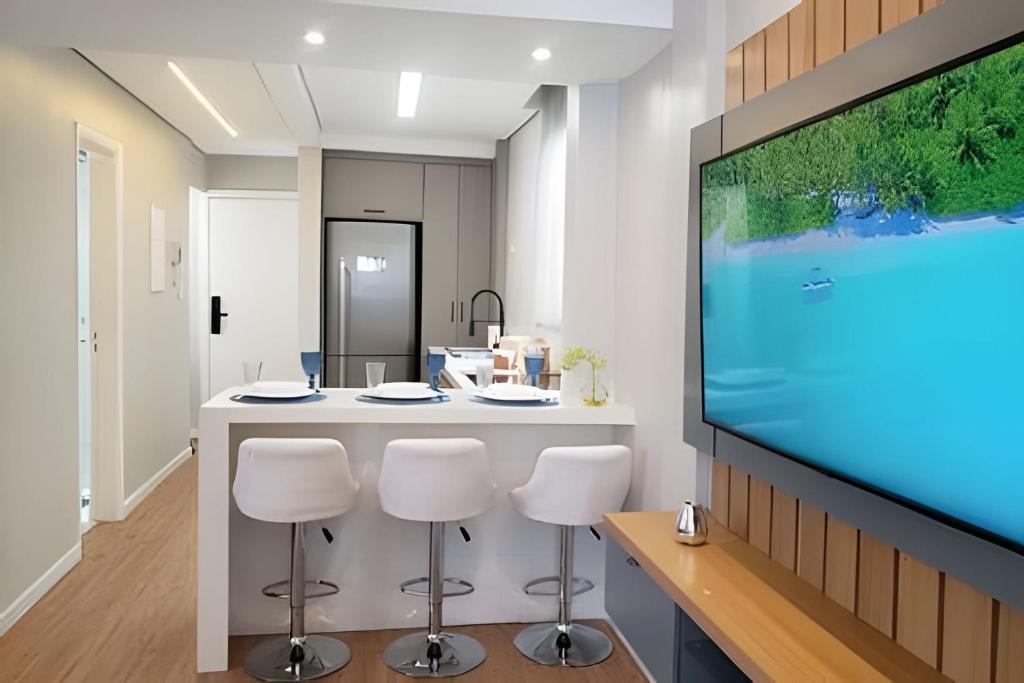 a kitchen with a bar with stools and a flat screen tv at Lindo e Moderno na praia do Gonzaga c/ar in Santos