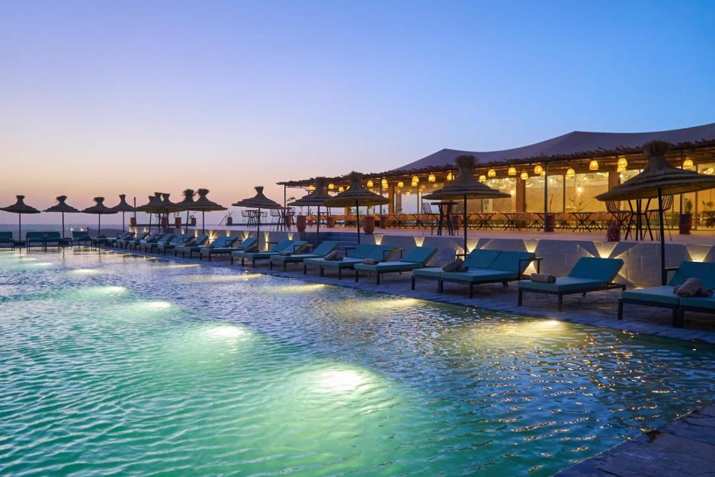 Una piscina con sillas y sombrillas en un resort. en Stellar Agafay Desert Camp, en Aït Daoud