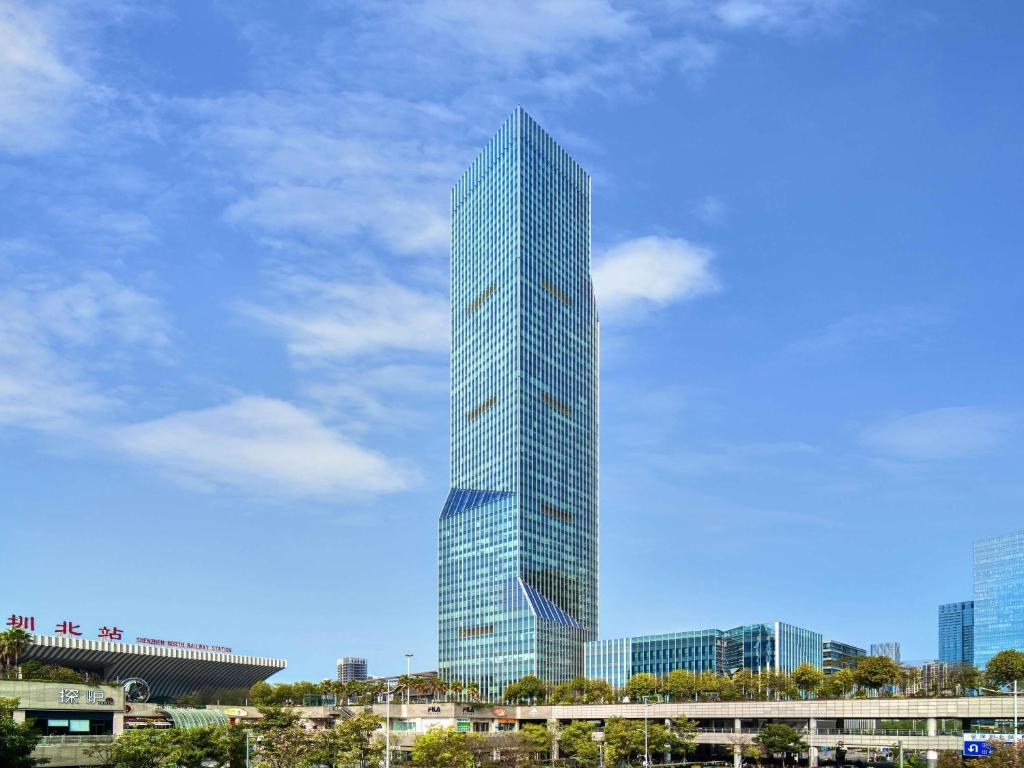 a tall glass skyscraper in a city at Pullman Shenzhen North in Shenzhen