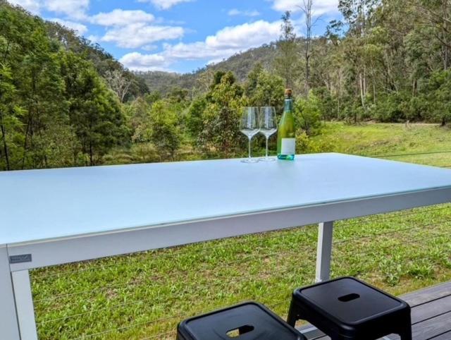 un tavolo con una bottiglia di vino e due sgabelli di The Burrows Off Grid Cabin, Unplug, Relax & Unwind a Wollombi