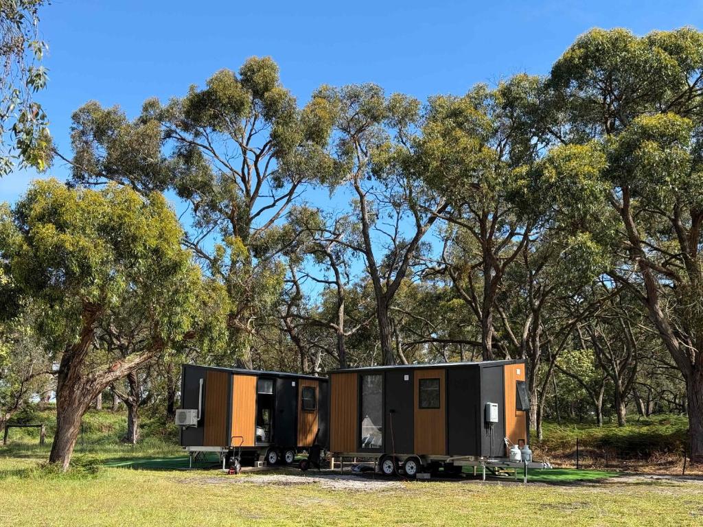 a trailer parked in a field next to trees at Bush Hideaway X by Tiny Away in Comaum