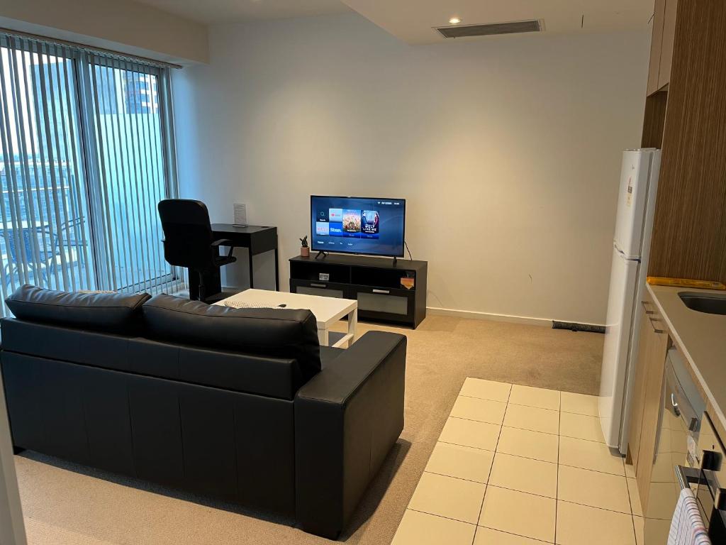 ein Wohnzimmer mit einer schwarzen Couch und einem Fernseher in der Unterkunft Tasha's Apartments on Morphett in Adelaide