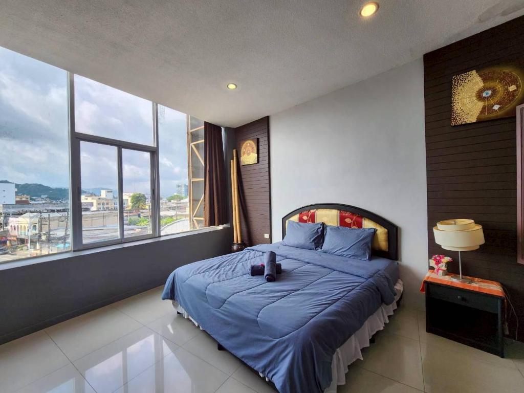 Schlafzimmer mit einem Bett mit blauer Bettwäsche und Fenstern in der Unterkunft The Rest Phuket in Phuket