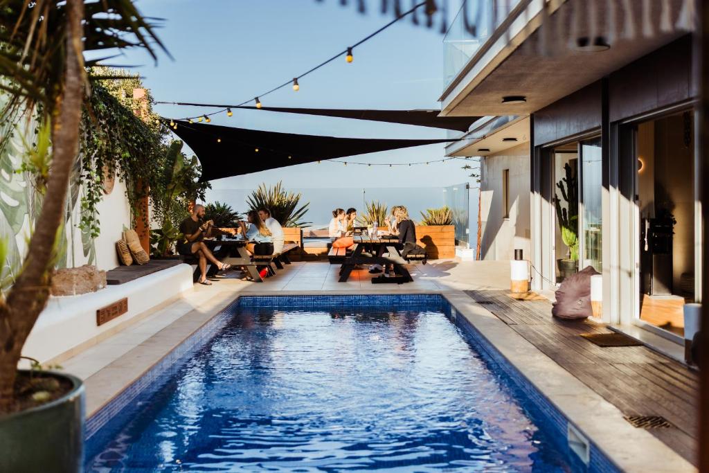 a swimming pool in a backyard with people sitting around tables at The Salty Surf & Yoga in Ericeira