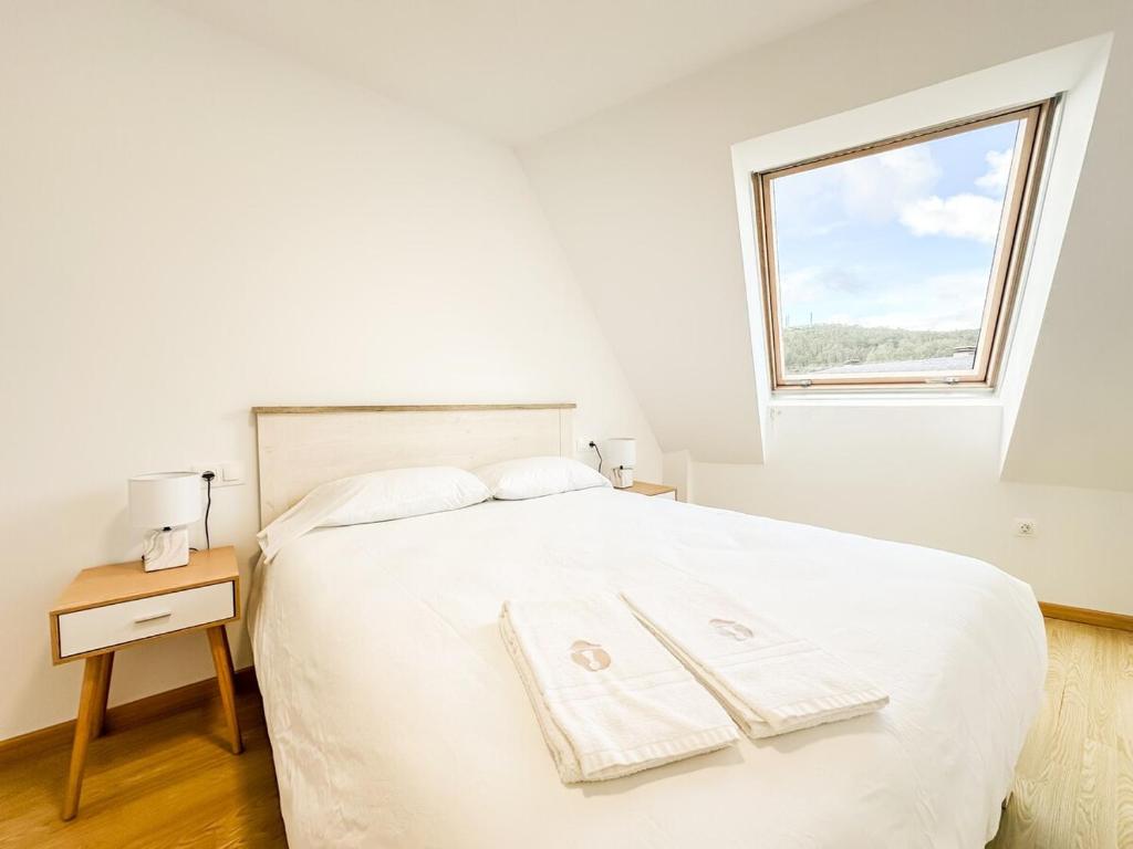 a white bedroom with a large white bed with a window at Apartamento Luzada by ALÔGA in Cee