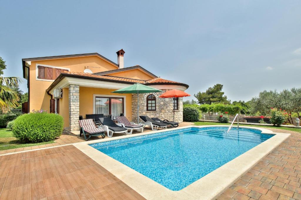 a pool with chairs and umbrellas in front of a house at Schöne Ferienvilla Morena Mit Pool in Kaštel