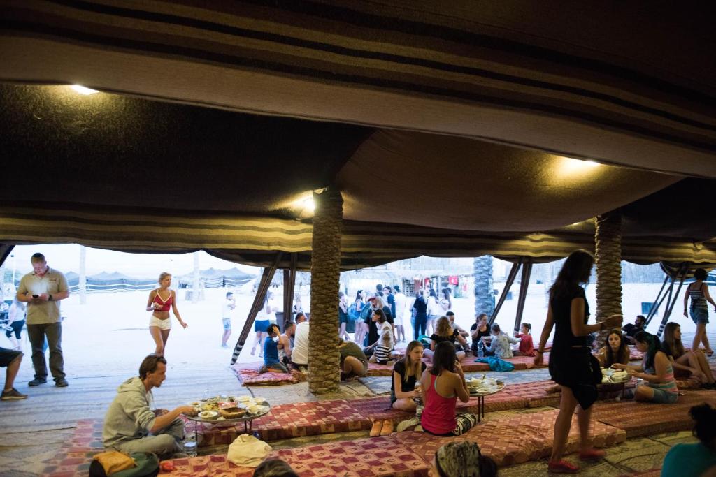 Eine Menschenmenge sitzt am Strand unter einem Zelt in der Unterkunft חאן השיירות- אוהלים בדואיים וקמפינג in Midreshet Ben Gurion
