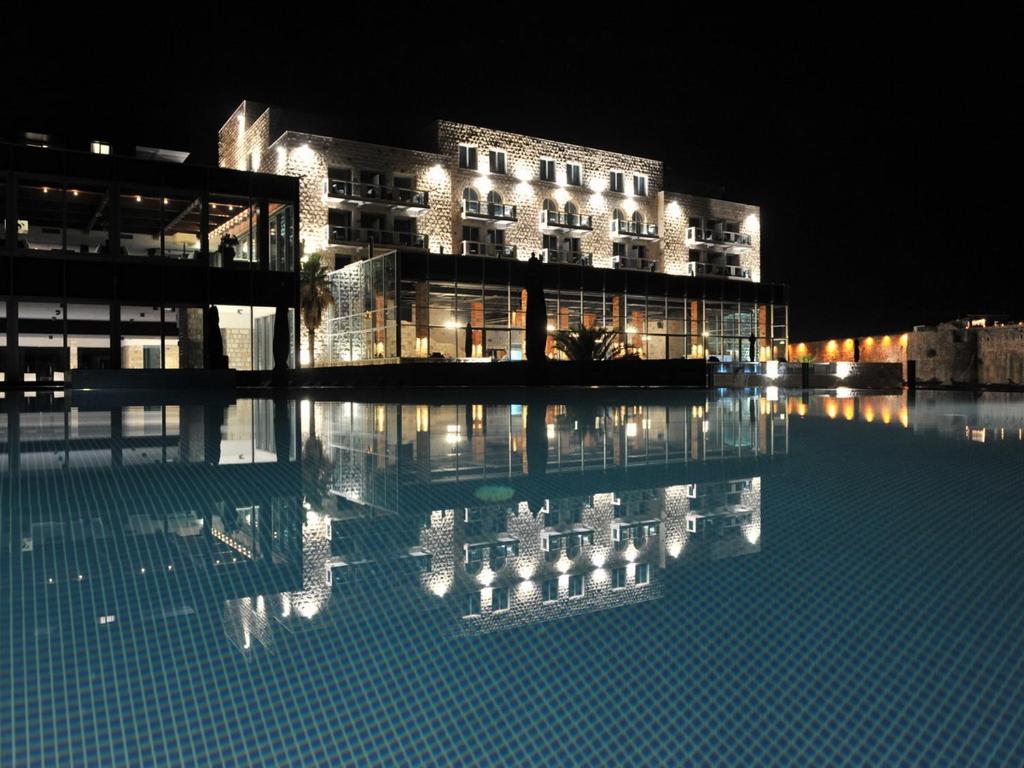 un bâtiment la nuit avec une réflexion dans l'eau dans l'établissement Avala Resort & Villas, à Budva