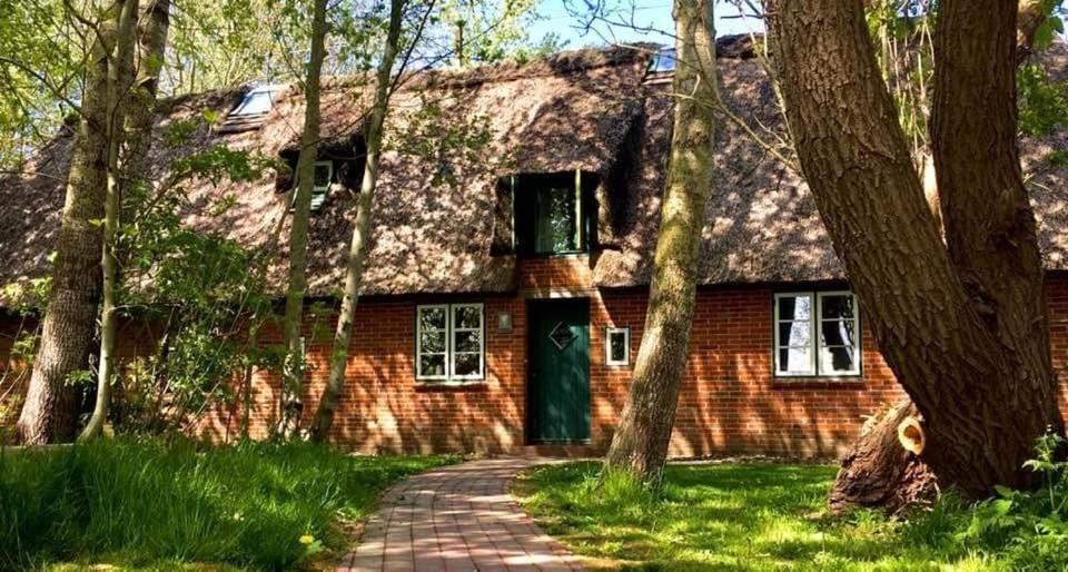 NorderfriedrichskoogReetdachhaus Für Erholsamen Familienurlaub的一座带绿门和树木的老砖屋