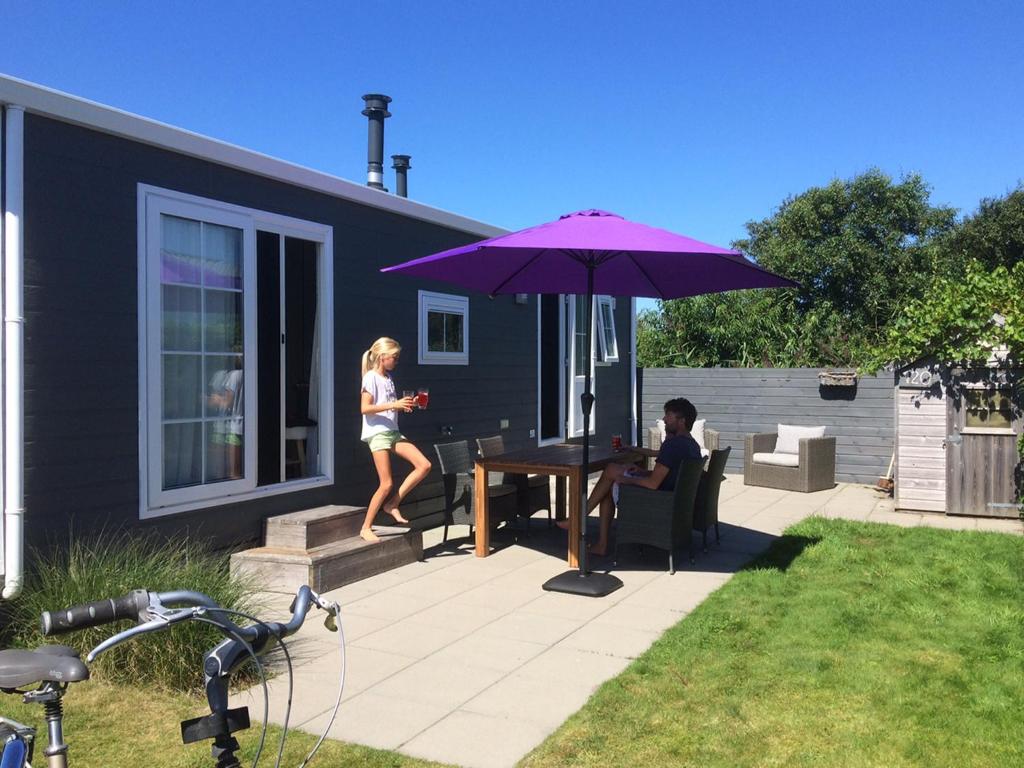 une femme debout sur une terrasse avec un parasol violet dans l'établissement Chalet Zilt Ameland, à Hollum