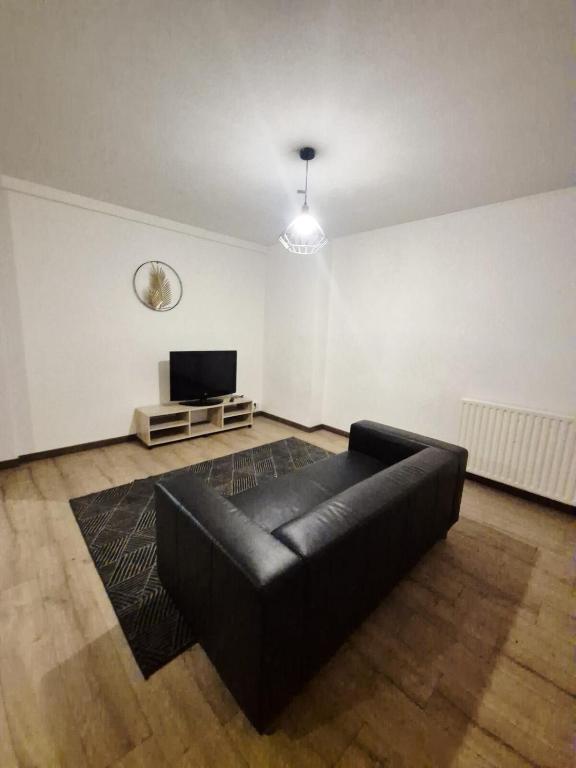 a living room with a black leather couch and a tv at Le Coty duplex - 5min chantier et 250m plage in Saint-Nazaire