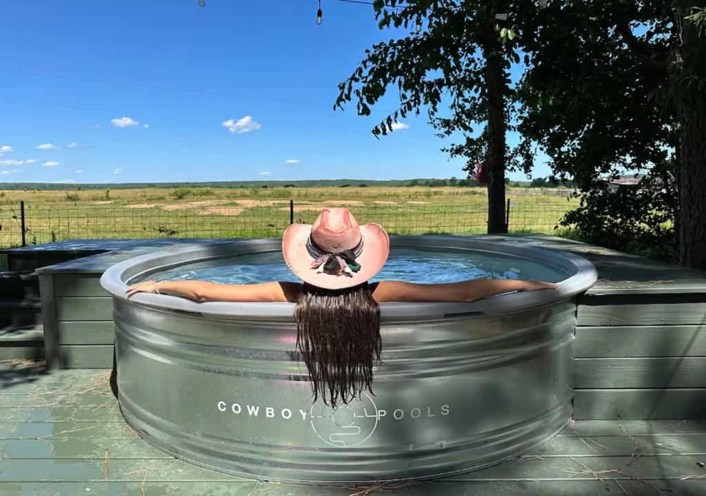 une femme portant un chapeau de rancher assise dans un jacuzzi dans l'établissement Sunrise, Mountain & Farm View - Heated Tub or Pool, à Mentone