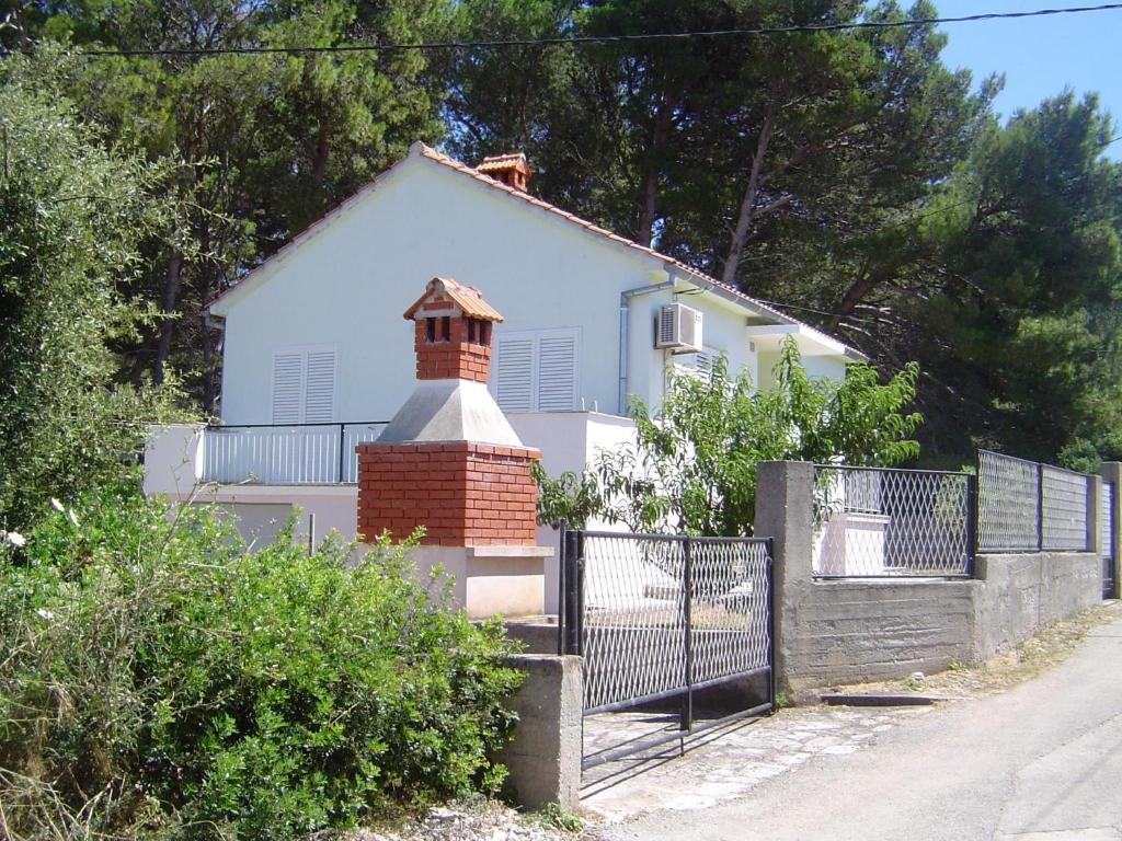 a white house with a brick chimney and a fence at Holiday House in Sušica