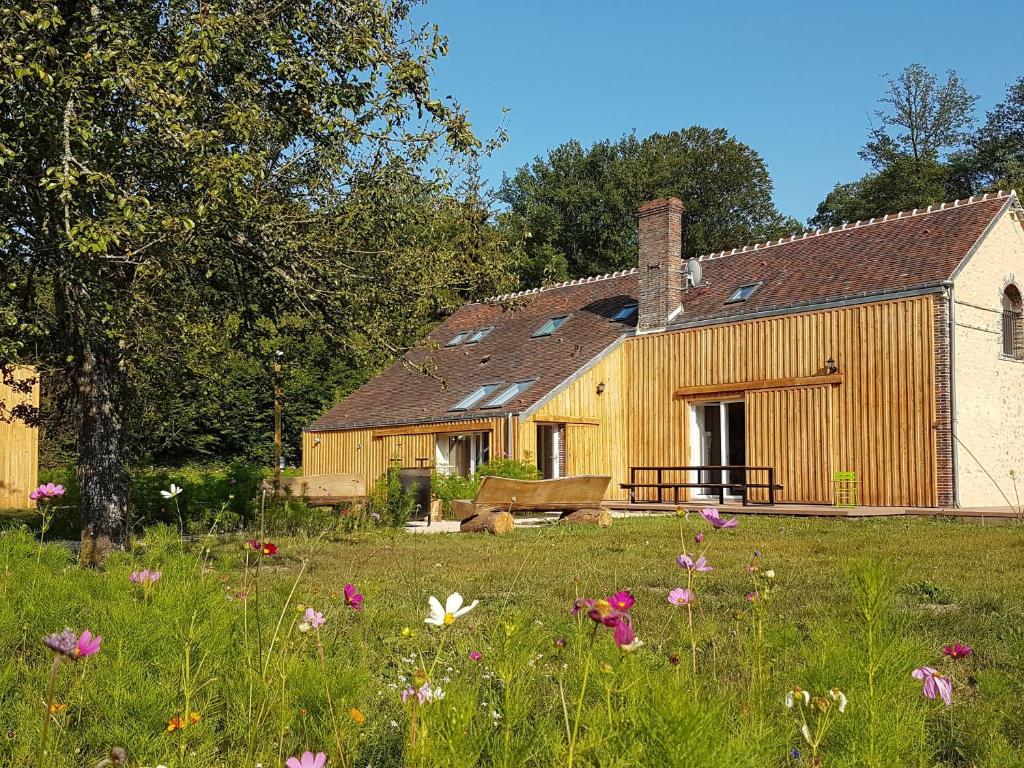 ein Holzhaus mit einem Blumenfeld davor in der Unterkunft Maison chaleureuse en forêt du Perche avec cheminée, jeux pour enfants et grand jardin - FR-1-581-51 in Senonches