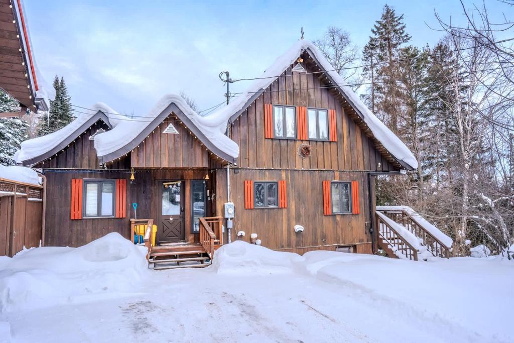 une maison en bois avec de la neige à l'avant dans l'établissement Sous Bois & Loft - Hot tub - Ski out, à Saint-Faustin–Lac-Carré