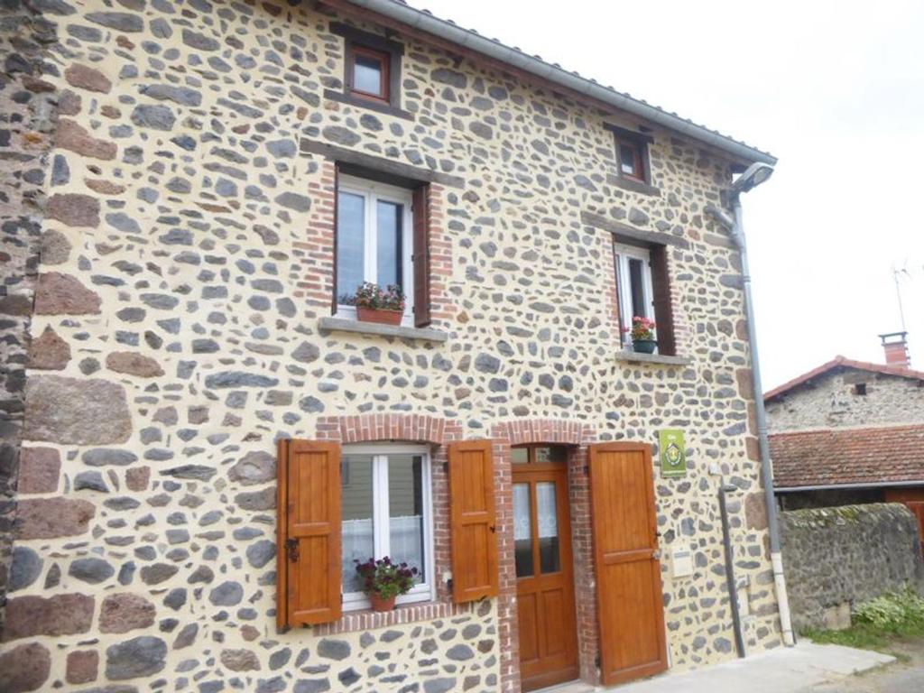 un bâtiment en pierre avec des fenêtres et des fleurs dessus dans l'établissement Maison de bourg restaurée avec cour privative au coeur d'un village paisible, proche gorges de l'Allier et sites historiques - FR-1-582-220, à Mazeyrat-Aurouze