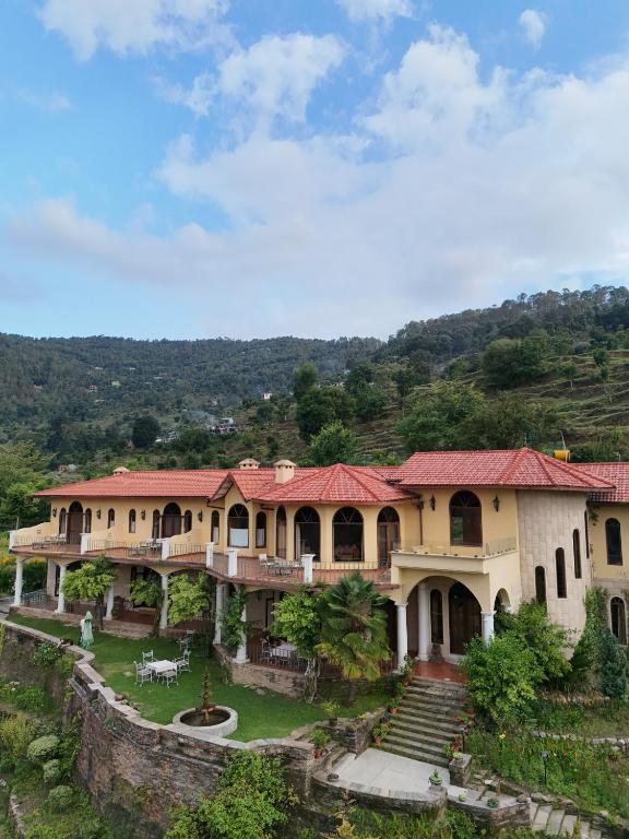 a large building with a red roof on a hill at The Orchard at Peora Estates in Mukteshwar