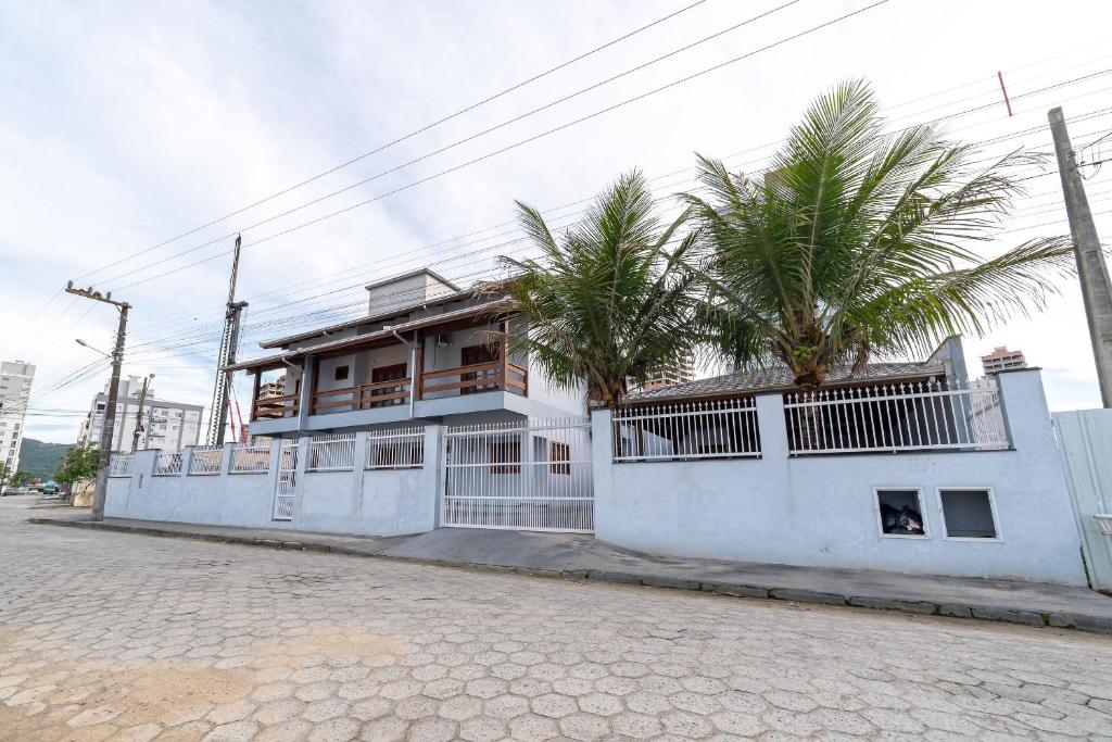 a white building with palm trees in front of it at Achei Itapema • Casa, 4 suítes + Área Gourmet in Perequê