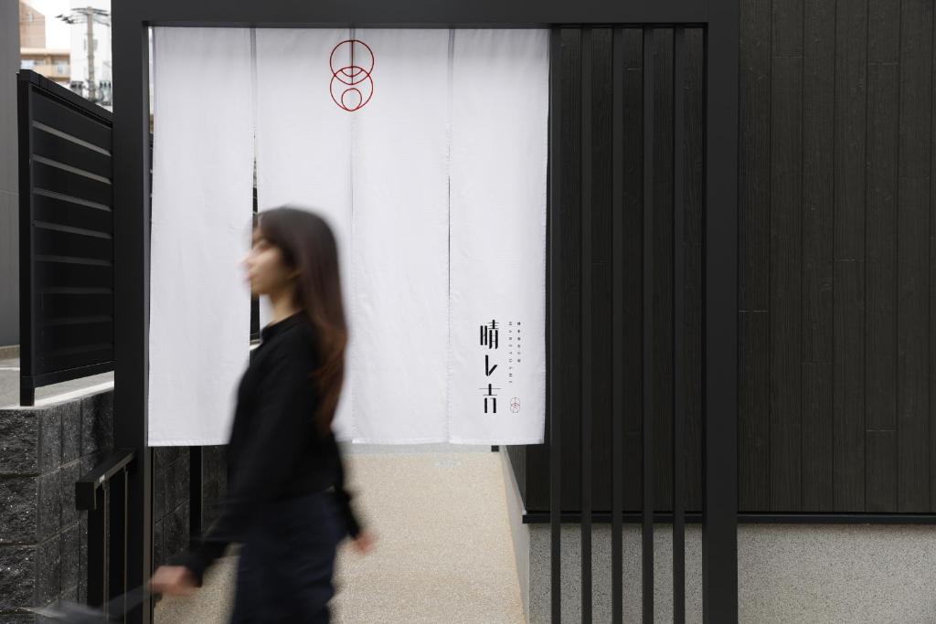 a woman walks past a wall with the olympics sign at 晴レ吉 in Fukuoka