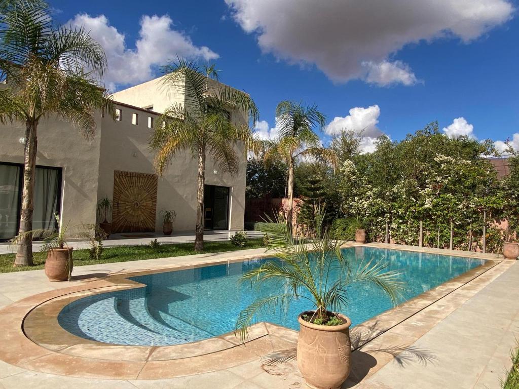 El Jemʼa GhematMagnifique Villa Proche Marrakech 4 Chambres, Piscine 10m, Accueille 8 à 10 Personnes的棕榈树环绕的房子前的游泳池