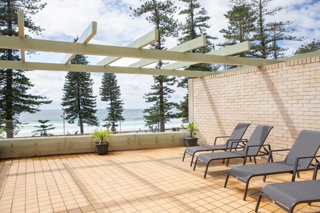a patio with chairs and a fence with a view of the ocean at Beachfront Manly Apartment With Balcony & Parking in Sydney