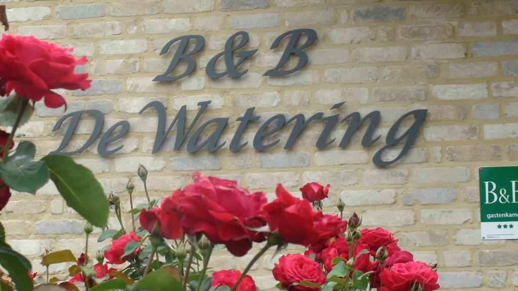 een bord op een stenen muur met rode rozen bij B&B De Watering in Lommel