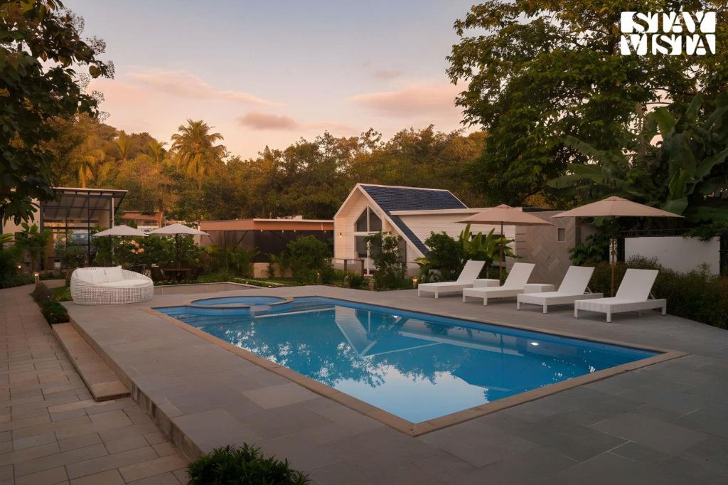 une piscine avec des chaises blanches et une maison dans l'établissement StayVista at Luma - 350 mtr from Mandwa Jetty, à Alibaug