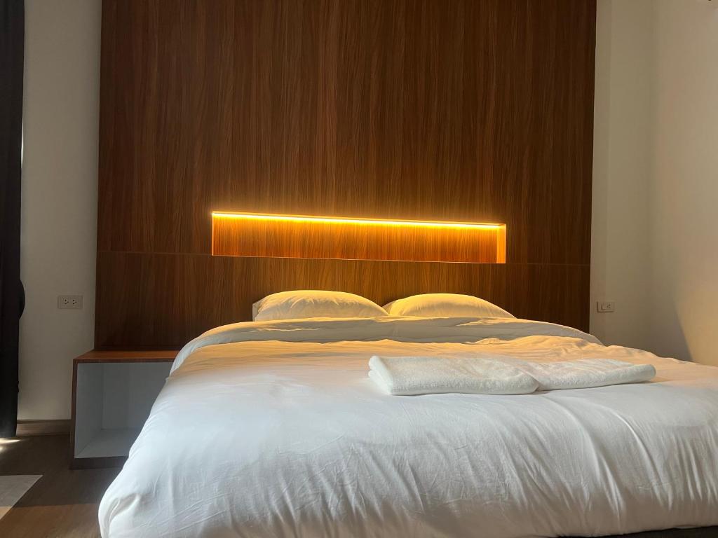a bedroom with a white bed with a wooden headboard at J&P Hotel Sriracha in Ban Hua Na