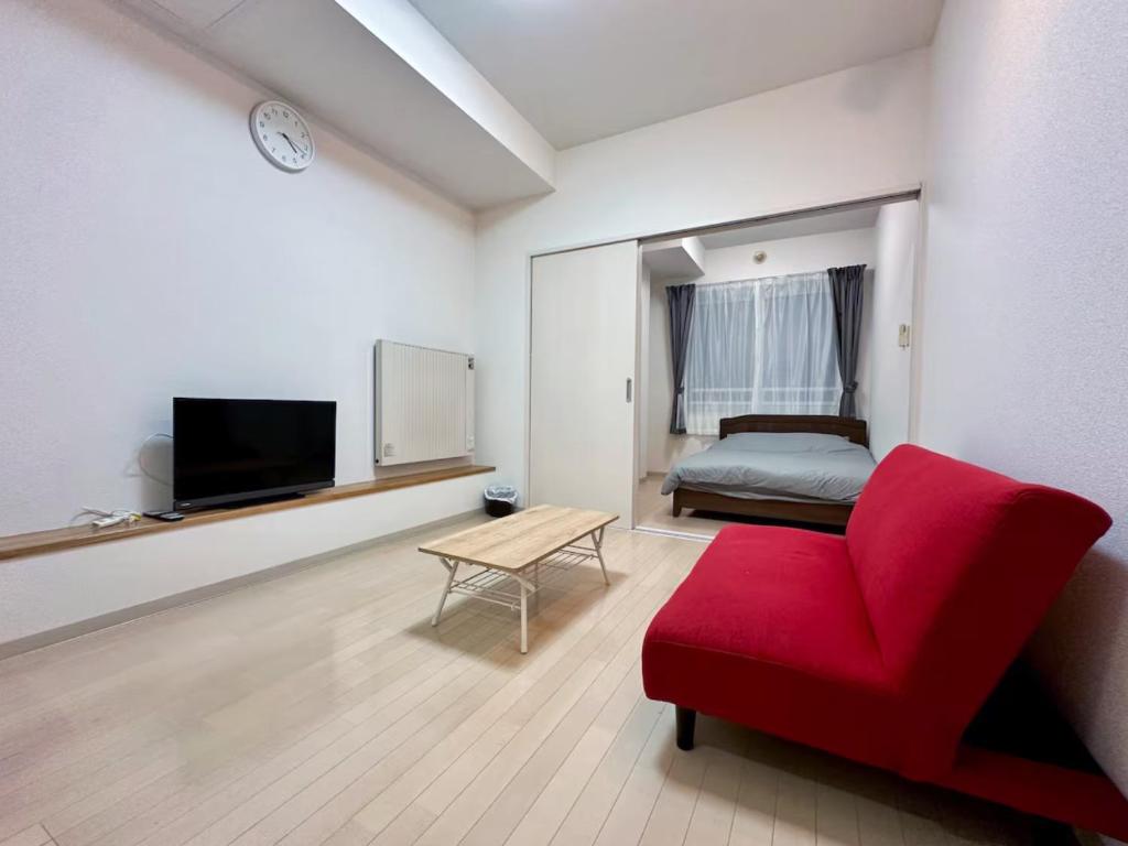 Una sala de estar con una silla roja y una cama. en 503好立地で札幌駅徒歩7分と大通駅徒歩6分で都心を満喫でき綺麗な部屋で快適が生活が実現, en Sapporo