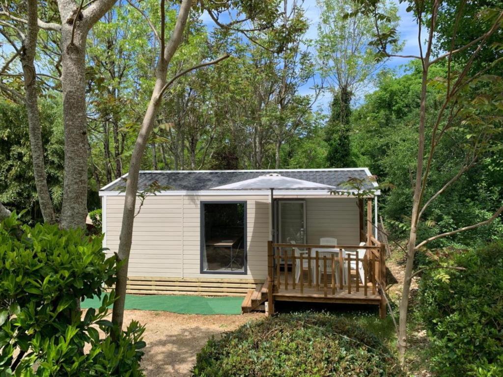 ein kleiner weißer Wohnwagen mit Veranda im Wald in der Unterkunft Mobilhome Malaga Climatisé 32 in Saint-Martial-de-Nabirat