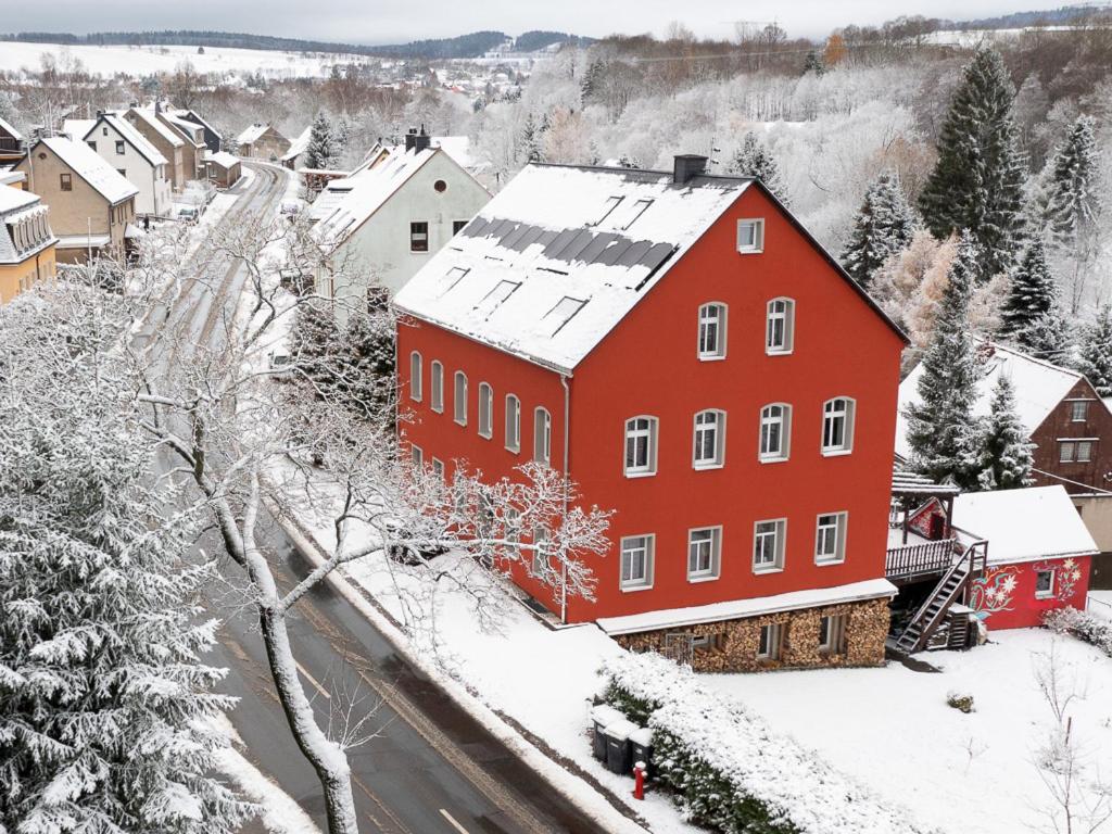 Un bâtiment rouge avec de la neige dans une ville dans l'établissement Erzgebirge Apartments Sehmatal, à Sehma