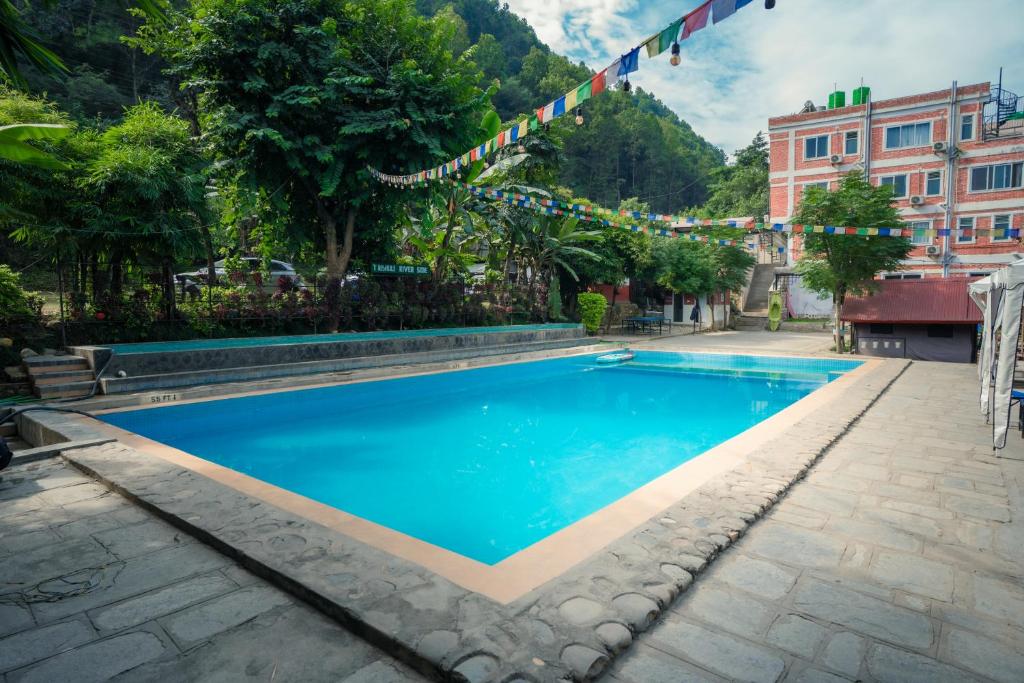 a blue swimming pool with flags and a building at Trishuli Riverside Resort in Benighāt