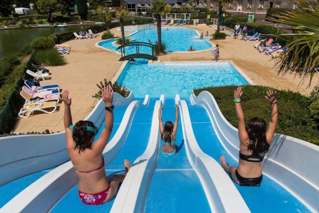 three girls are going down a water slide at a resort at ZEcamping 4 étoiles familial avec étang de pêche et piscine chauffée in La Haye-du-Puits