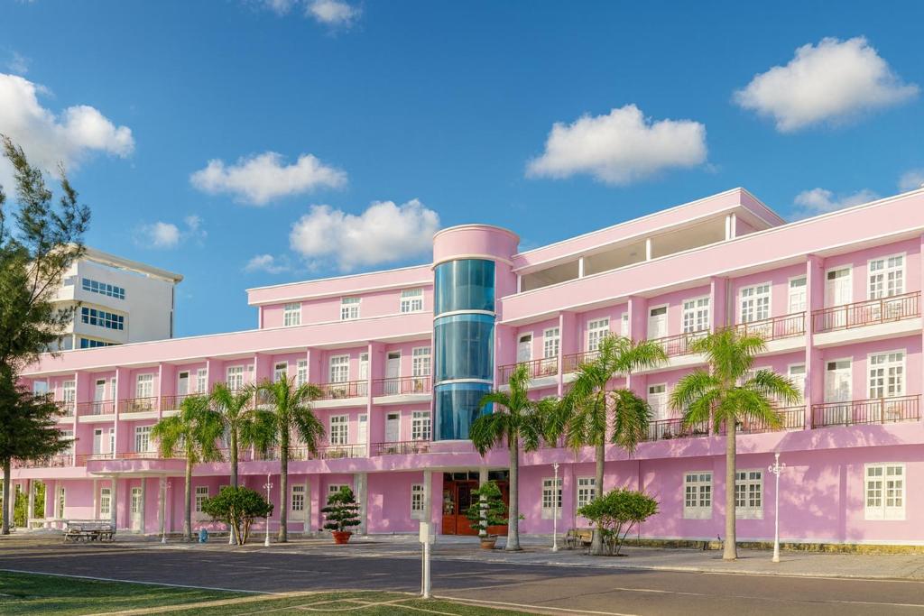 un bâtiment rose avec des palmiers devant lui dans l'établissement Khu Nghỉ Dưỡng Đoàn 298 - Khách Sạn 3 Tầng, à Long Hải