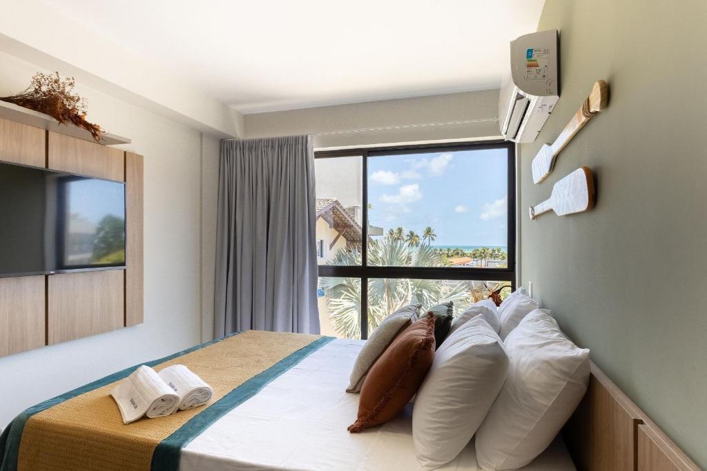 a bedroom with a bed with white pillows and a window at Season Smart Flats by BLU stay in Porto De Galinhas