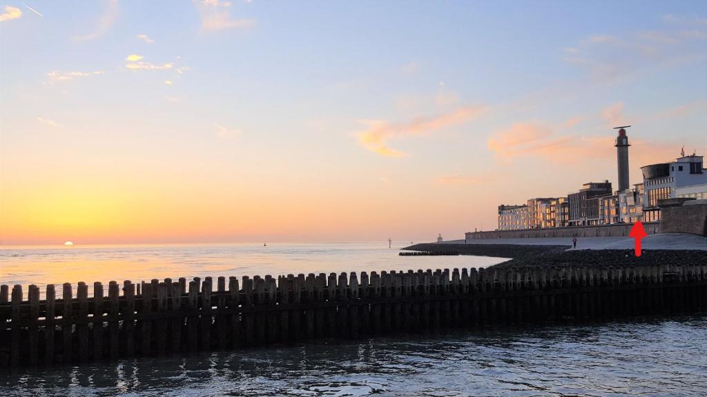 a pier with a lighthouse and the ocean at sunset at Studio Zeezicht in Vlissingen
