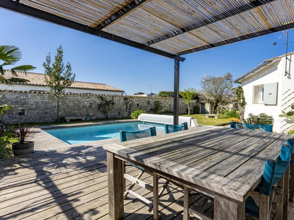 a patio with a wooden table and chairs next to a swimming pool at Maison familiale avec piscine pour 9 personnes - FR-1-835-4 in Le Bois-Plage-en-Ré