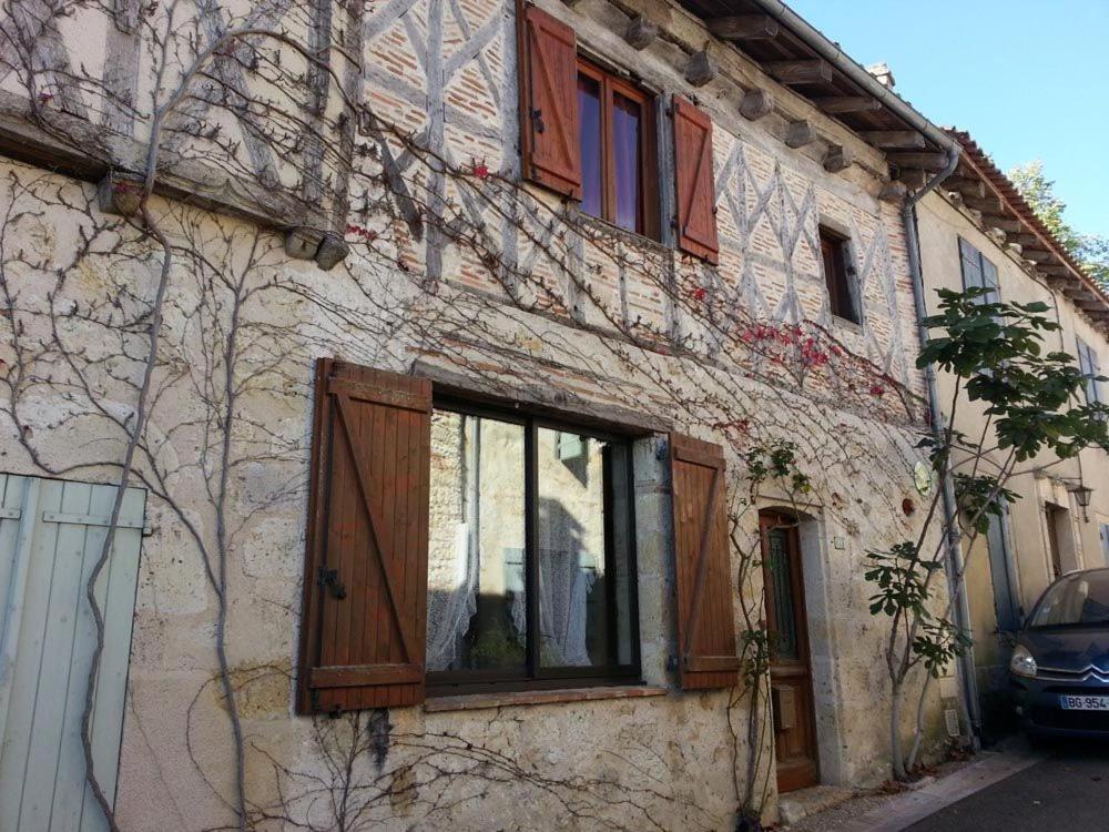 Un edificio con ventanas de madera y un coche aparcado al lado. en Gîte près de l'auberge, en Saint-Antoine