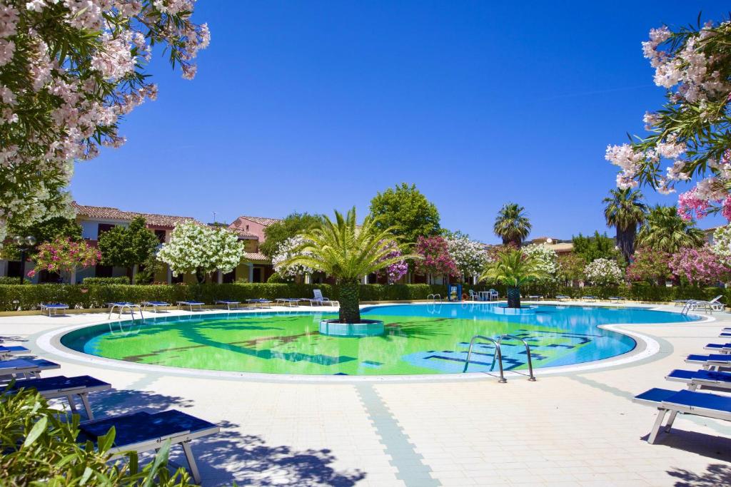 - une piscine avec des chaises et des arbres dans un complexe dans l'établissement Residence Oasi Anfiteatro, à Porto Ottiolu