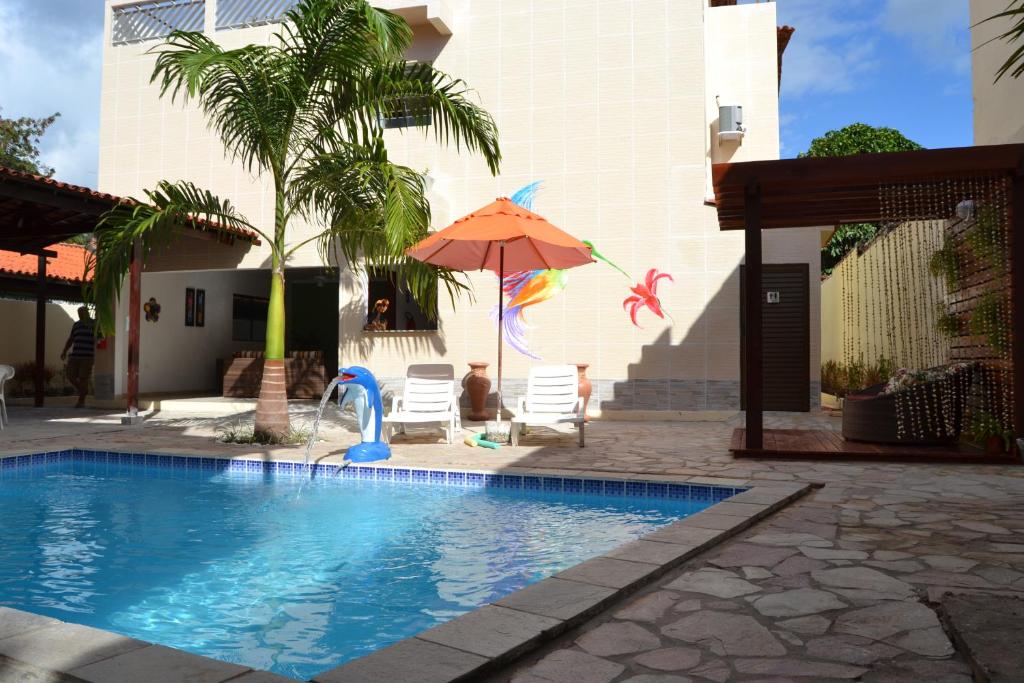 uma piscina com um guarda-sol e cadeiras e uma palmeira em Pousada Beija Flores em Porto de Galinhas