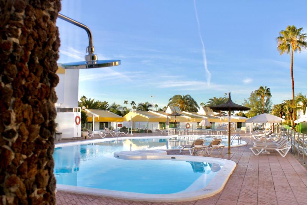 a pool at a resort with chairs and umbrellas at Vega Maspalomas - Escapada de sol, piscina y relax in San Bartolomé