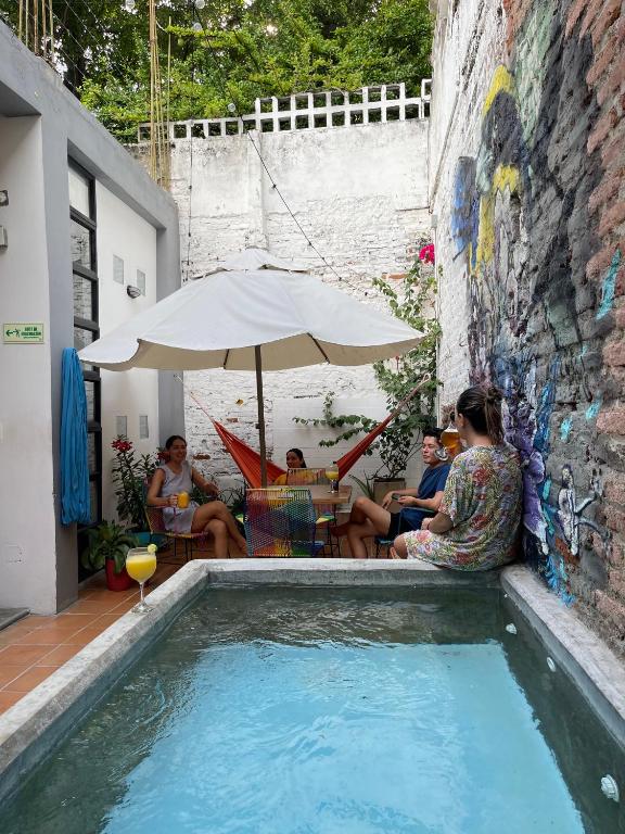 a group of people sitting under an umbrella next to a pool at Imagine hostel in Santa Marta