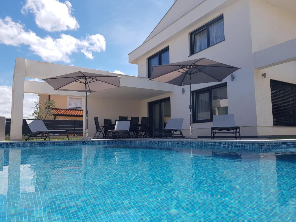 - une piscine en face d'une maison avec des parasols dans l'établissement Ferienhaus Mit Privatem Pool In Ruhiger Lage, à Kaštel