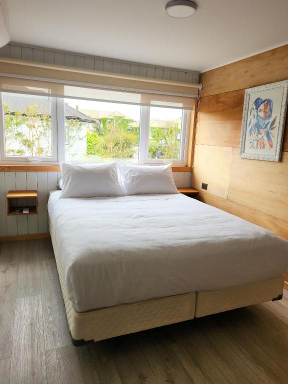 1 Schlafzimmer mit einem großen weißen Bett und 2 Fenstern in der Unterkunft suites puerto varas camino al corazon in Puerto Varas