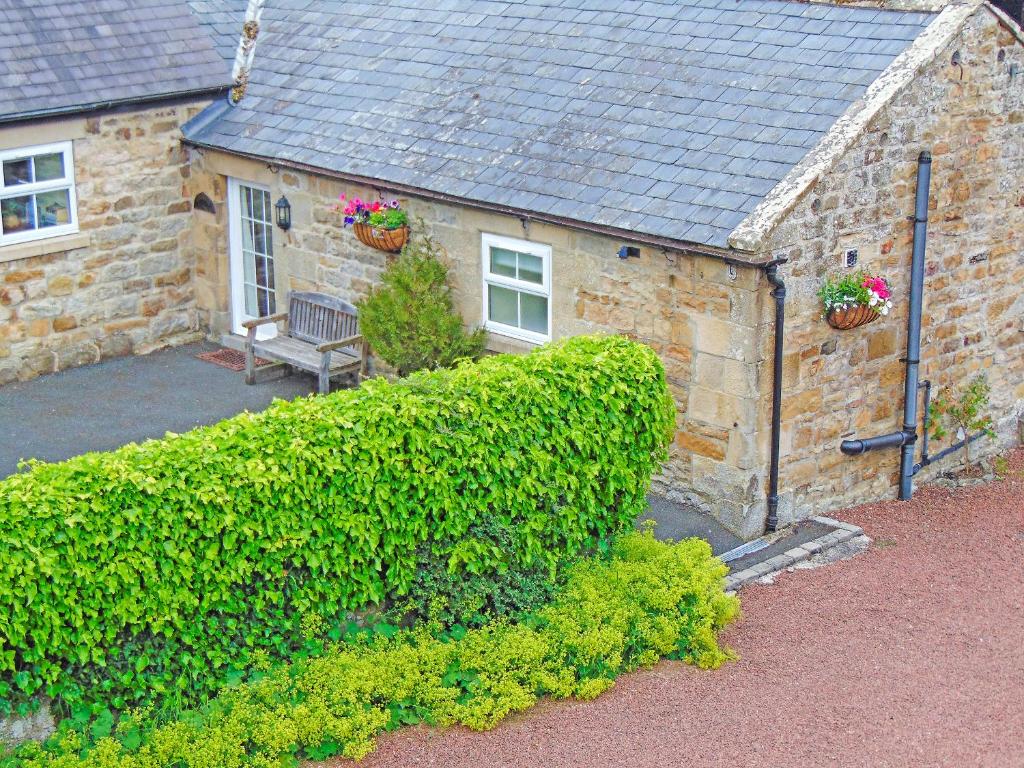 ein Steinhaus mit einer Bank und einer Hecke in der Unterkunft Grooms Cottage in Elsdon