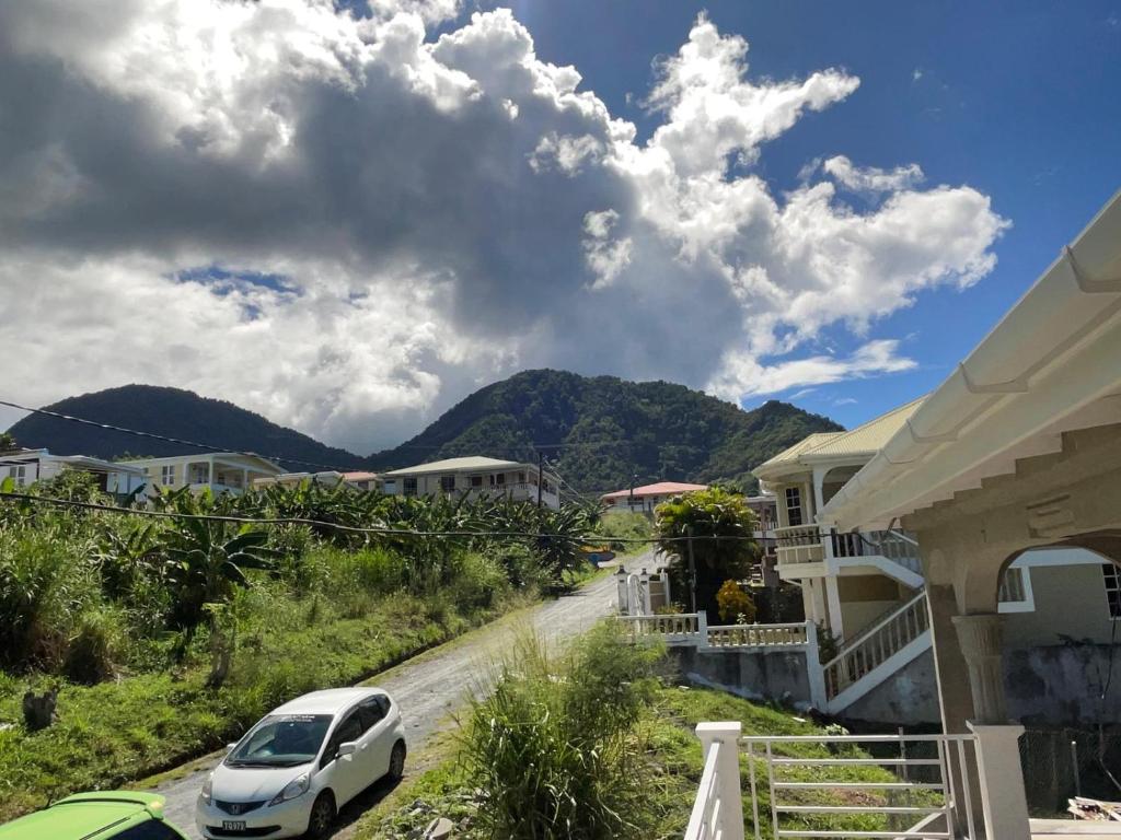 a white car parked on a road next to houses at Kingdom Rentals - AirBnCar in Roseau