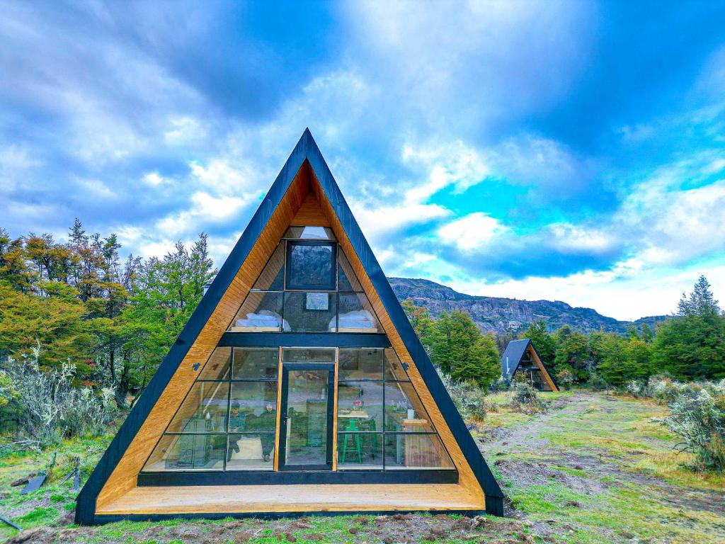 塞罗别墅卡斯蒂略OUTSCAPE l Preciosa Cabaña en Villa Castillo的田野里一座三角形的房子，窗户是玻璃的。